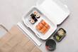 Plastic container with tasty sushi rolls, chopsticks and paper bag on grey grunge background. Delivery concept