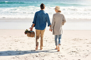 Wall Mural - Holding hands, beach and couple in walking, back and holiday for vacation, ocean and adventure. Romantic, summer and picnic basket in bali, bonding and sea or outdoor, mockup and romance on sand