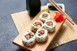 Board with tasty sushi rolls, marinated ginger and bamboo mat on black grunge background, closeup