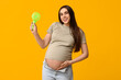 Pregnant young woman with small electric fan on yellow background