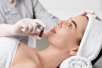 Canvas Print - Professional cosmetologist holding skincare ampoule while working with client in clinic, closeup