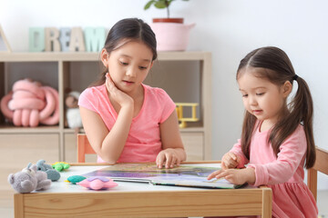 Poster - Cute little Asian happy sisters with toys reading book at table in child room