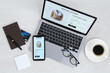 Online store website on laptop screen. Computer, smartphone, stationery, glasses and coffee on light grey wooden table, flat lay