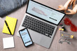 Online store website on laptop screen. Computer, smartphone, shopping cart, stationery and accessories on grey table, flat lay