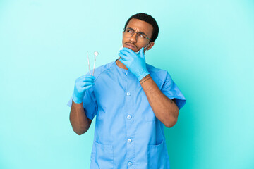 Wall Mural - African American dentist holding tools over isolated blue background having doubts