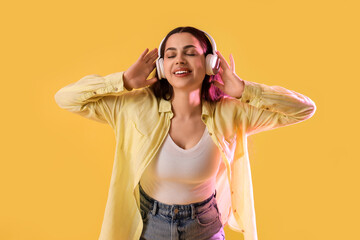 Canvas Print - Beautiful young happy woman in headphones listening music on yellow background