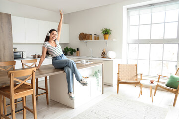 Poster - Beautiful young happy woman in headphones listening music at kitchen