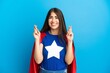 Super Hero caucasian woman isolated on blue background with fingers crossing