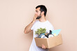 Man holding a box and moving in new home over isolated background covering mouth and looking to the side