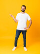 © luismolinero - Full-length shot of man with beard over isolated yellow background pointing finger to the side