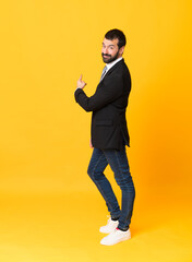 Wall Mural - Full-length shot of business man over isolated yellow background pointing back