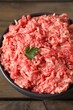 Raw ground meat and parsley in bowl on wooden table, closeup
