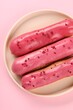 Delicious eclairs covered with glaze on pink background, top view