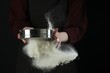 Woman sieving flour against black background, closeup