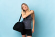 Young sport woman with sport bag isolated on blue background suffering from pain in shoulder for having made an effort