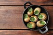 Delicious cooked snails in baking dish on wooden table, top view. Space for text