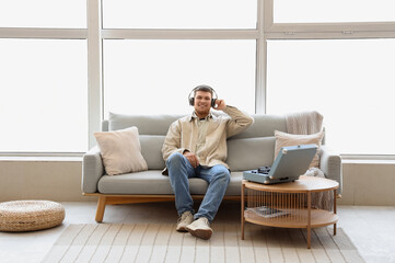 Canvas Print - Young man in headphones with record player listening to music on sofa at home