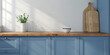 Encimera de cocina de madera en color azul, sobre la que se encuentran dos tablas de cortar de madera y un pequeño jarrón con planta de interior, sobre pared blanca