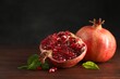 Fresh pomegranates and green leaves on wooden table, space for text