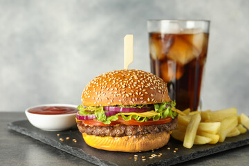 Wall Mural - Burger with delicious patty, soda drink, french fries and sauce on dark table against gray background, closeup