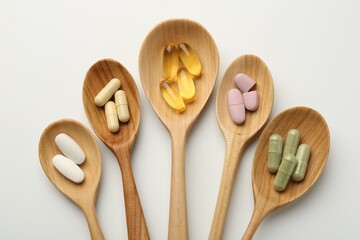 Vitamin capsules in wooden spoons on white background, flat lay