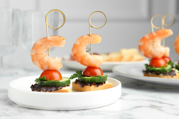 Tasty canapes with shrimps, cucumber, greens and tomatoes on white marble table, closeup