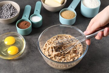 Woman making dough with chocolate chips at grey table, closeup