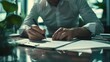 © chanidapa - Corporate Contracts: Businessperson diligently signing paperwork at a modern desk in a corporate environment.