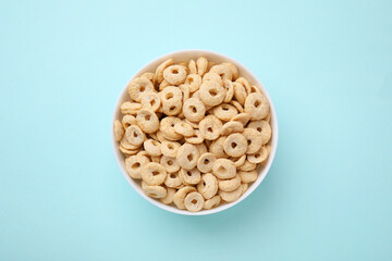 Wall Mural - Tasty cereal rings in bowl on light blue table, top view