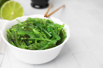 Tasty seaweed salad in bowl on white tiled table, closeup