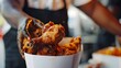 Close-up of a hand reaching into a paper bucket, fingers poised to grasp a piece of perfectly fried chicken