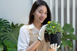 Beautiful young woman spends her weekends tending to the plants in her garden, carrying a plant bag, preparing to transplant it into a pot, looking at camera