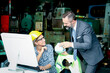 © Stella - ฺฺBeautiful woman industrial engineer worker wears helmet and safety glasses using computer to discuss with businessman, people work at manufacturing plant industry factory, boss and secretary talking