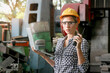© Stella - Beautiful industrial female engineer with helmet and safely glasses holding walkie talkie during using a laptop computer at manufacturing plant factory, young woman worker working in industry factory.