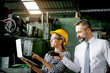 © Stella - Young beautiful woman industrial engineer worker with helmet and safety glasses using laptop computer during discussing with senior businessman manager, people work at manufacturing industry factory