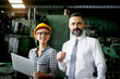 © Stella - Young beautiful woman industrial engineer worker with helmet and safety glasses using laptop computer during discussing with senior businessman manager, people work at manufacturing industry factory