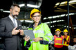 © Stella - Beautiful woman industrial engineer worker wearing safely helmet and protective clothing, holding tablet and discussing with her senior businessman manager, at heavy industry manufacturing factory