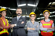 © Stella - Senior businessman manager with industrial engineer women with safety helmet stand in line at manufacturing industry factory. Group of industrial workers and boss stand with arms crossed at workplace.