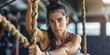 © ckybe - A strong Latina is scaling a rope at the gym with determination, donning a ponytail and athletic attire.