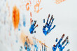 The paint of hands and drawing of kids craft show artist skill using blue and orange color in drawing class that stained on the white wall. Focus right side of picture, left side blurry. Erudition.