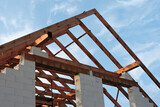Fototapeta Zwierzęta - A timber roof truss in a house under construction, walls made of autoclaved aerated concrete blocks, rough window openings, a reinforced brick lintel, a scaffolding, blue sky in the background