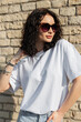 Cool curly beautiful fashion girl in a stylish white mock-up T-shirt on a background of a brick wall in the sunlight