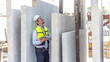 © Ron - Male engineer checks quality of readymade floor or wall in a factory. Technician with safety hat stands next to a pile of concrete walls.