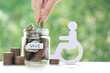Man on wheelchair and coin money in the glass bottle on natural green background,Save money for prepare in future and handicapped person concept
