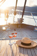 Romantic picnic with wine on a yacht in sea. Summer travel at sunset. Two wineglasses with cherry, straw hat on wooden deck. Alcohol-free drink on vacation. Beautiful authentic holidays, aesthetics