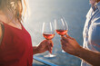 Drinking wine by sea. Two wineglasses in hands of couple in love at sunset beach. Man and woman traveling on yacht, enjoying summer vacation. Romantic celebration on open-air restaurant terrace