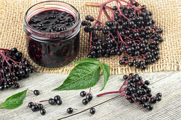 Wall Mural - Fresh ripe black elderberries, elderberry syrup and leaves of elderberry on rustic wooden board. Alternative medicine and lifestyle.