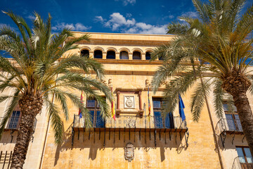 Canvas Print - Facade between palm trees of the Elche Town Hall in Elche, Alicante, Valencian Community, Spain, in daylight