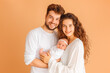 © VisualProduction - Portrait of young happy man and woman holding newborn cute babe dressed in white unisex clothing.