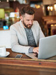 Businessman, laptop and phone in coffee shop for email, conversation and communication with client. Male person, technology and remote work in cafe for brainstorming, planning and idea for project